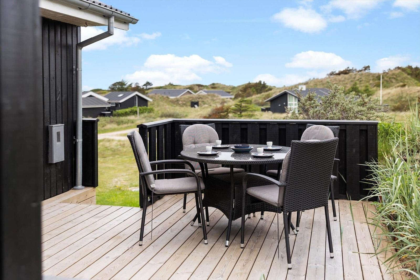 Deck with table and chairs, view of hills and houses.