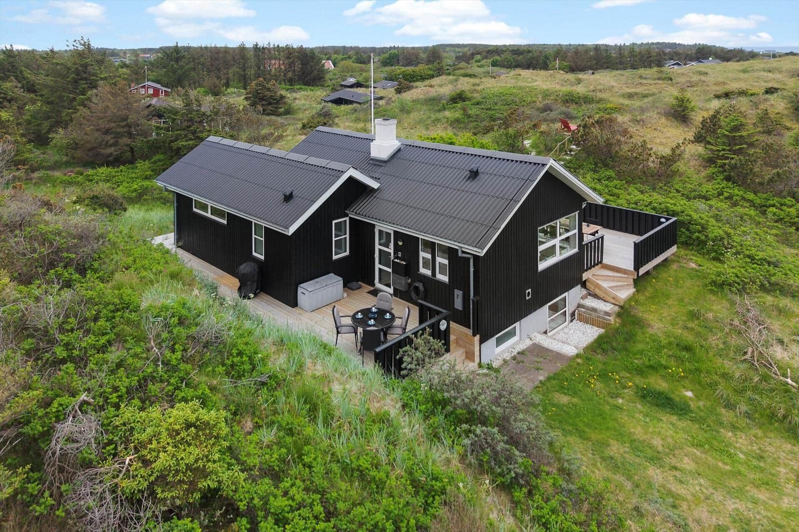 Black house with terrace and garden in green surroundings.