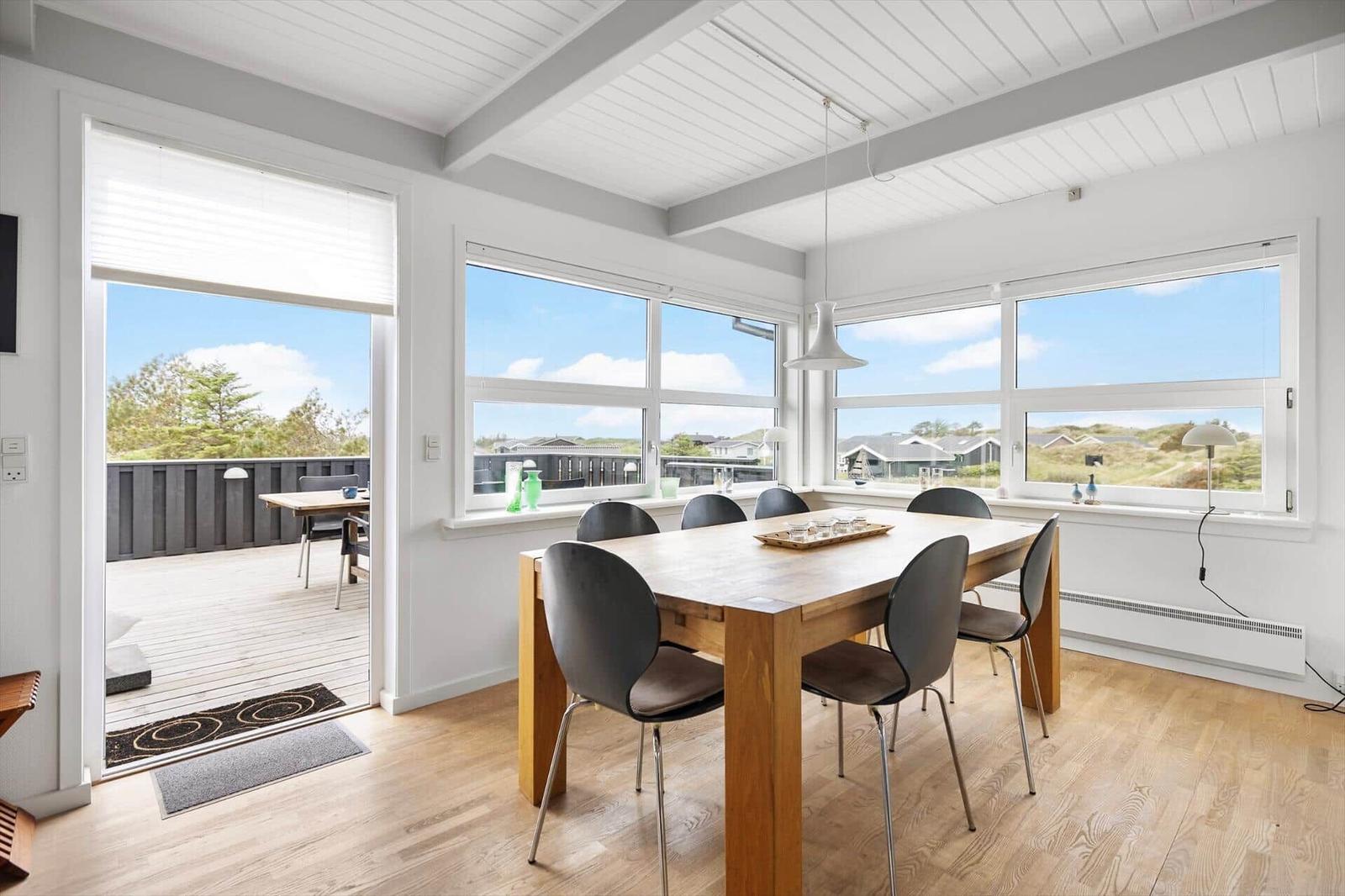 Dining room with wooden table, chairs, and view of balcony and landscape.