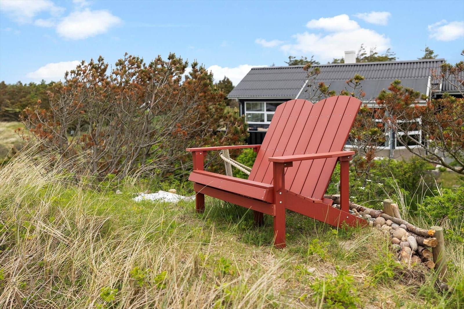 Red garden chair on grassy area in front of modern house with roof and windows.