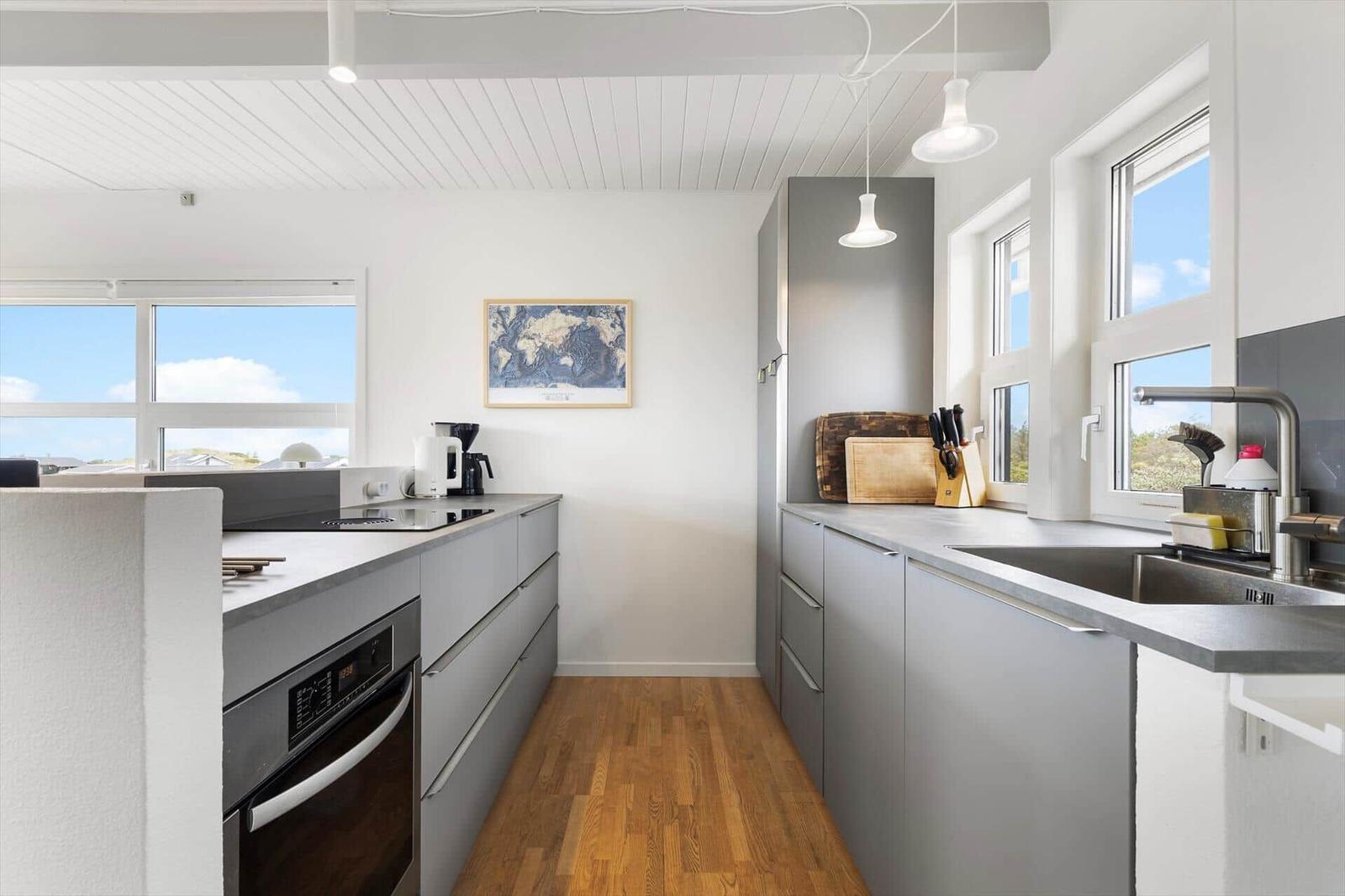 Modern kitchen with gray cabinets, wooden floor, and large windows with view.