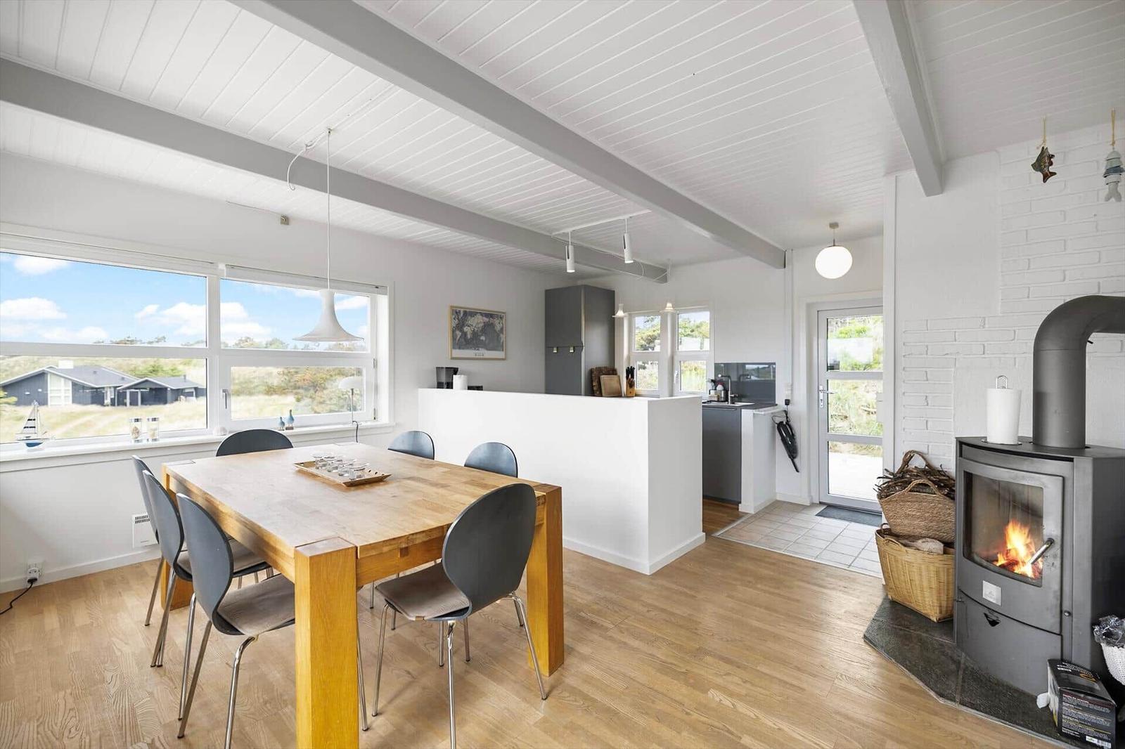 Dining area with wooden table and chairs, kitchen, and wood-burning stove with fire.