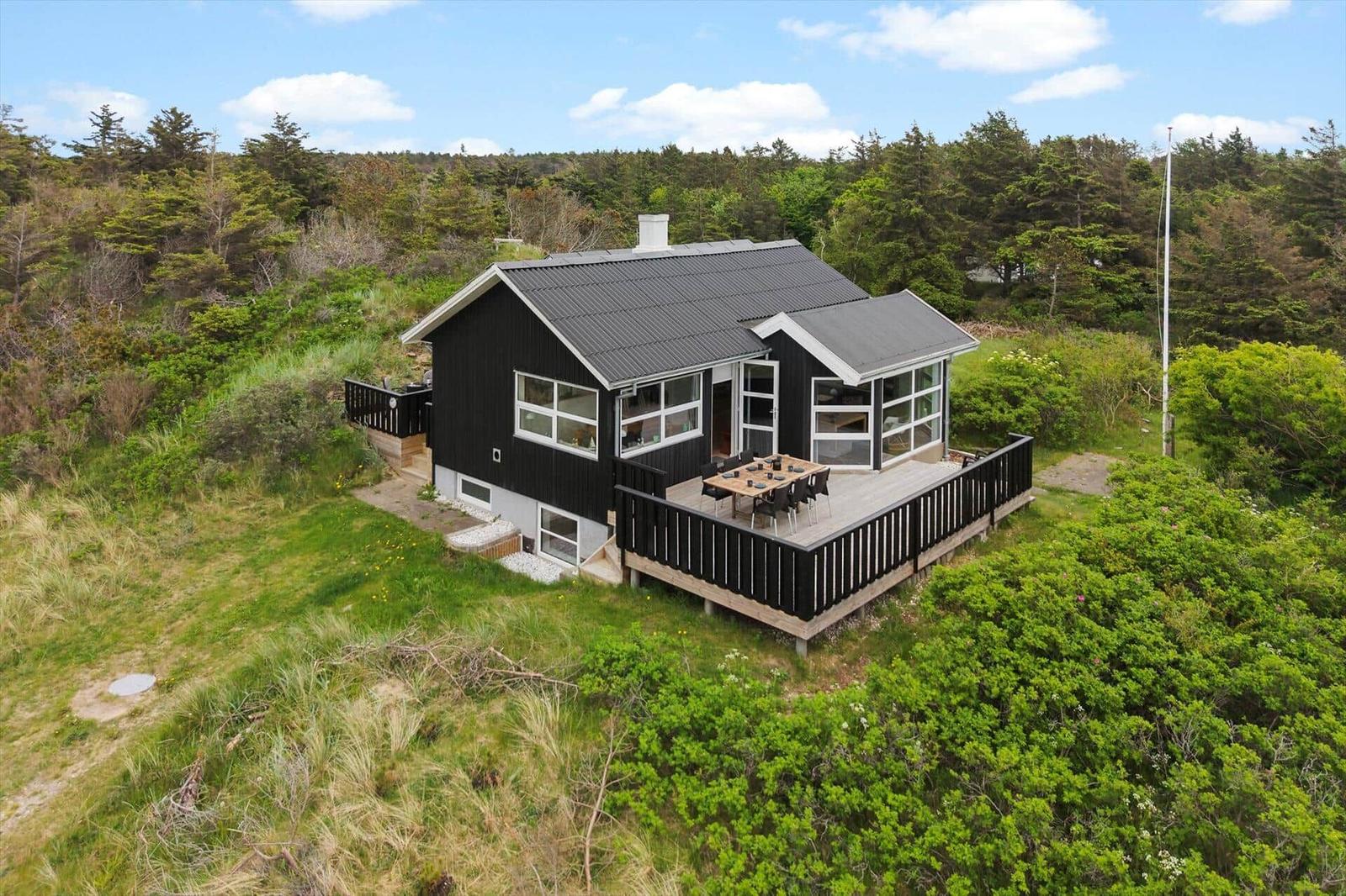 Black house with terrace and garden in green surroundings.