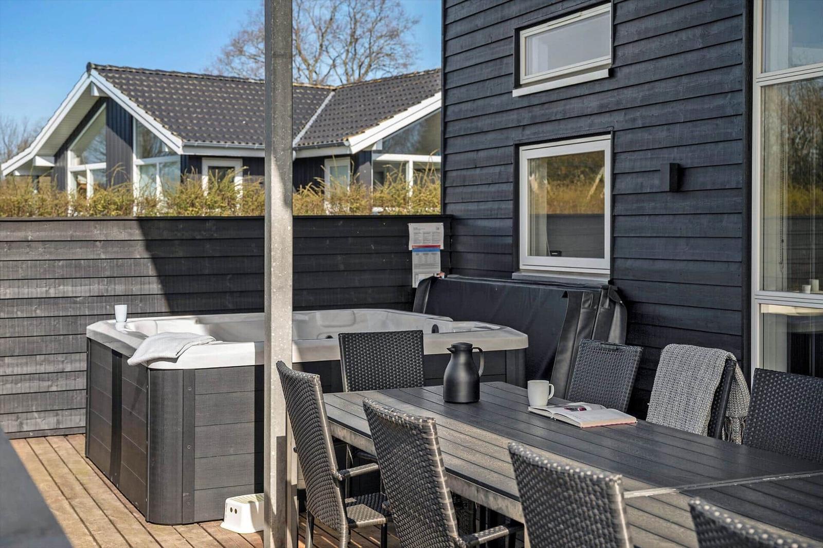 Deck with hot tub and dining table with chairs in front of dark gray siding.