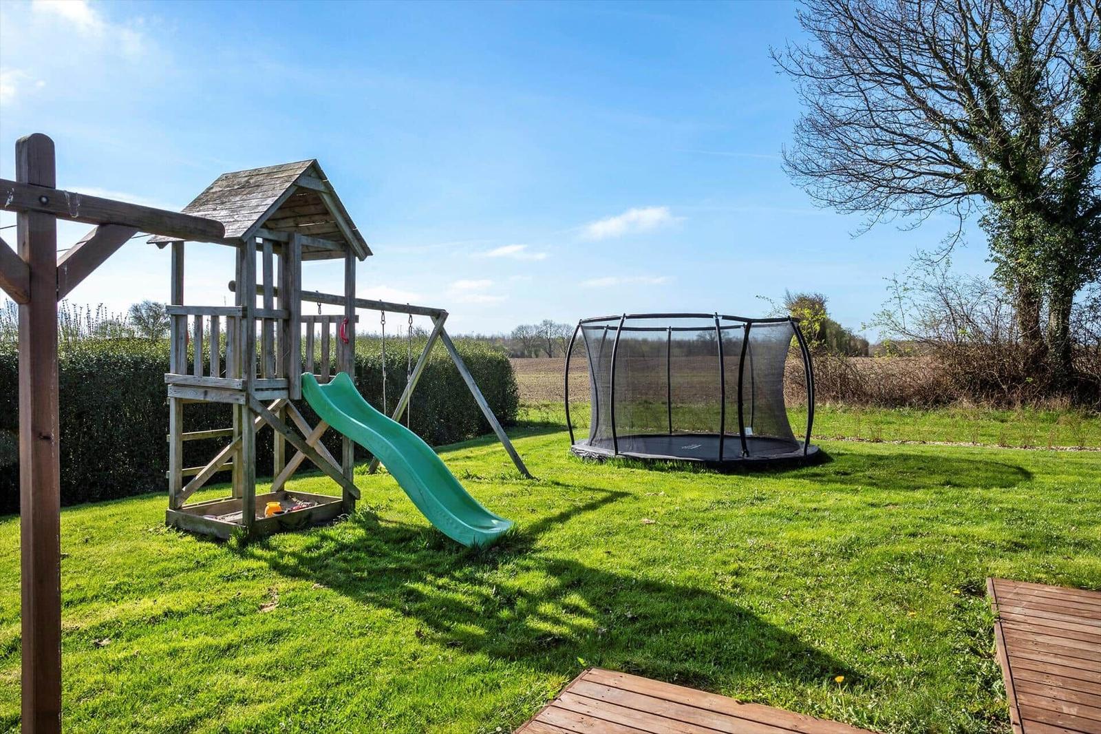 Backyard with playhouse and trampoline on green lawn.