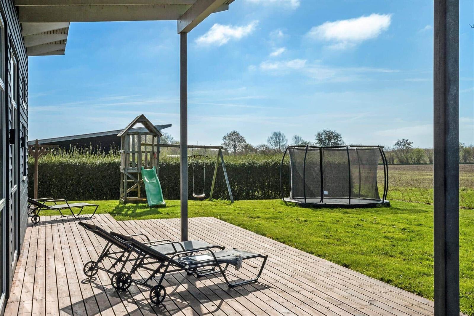Deck with lounge chairs, playground, and trampoline in the garden.