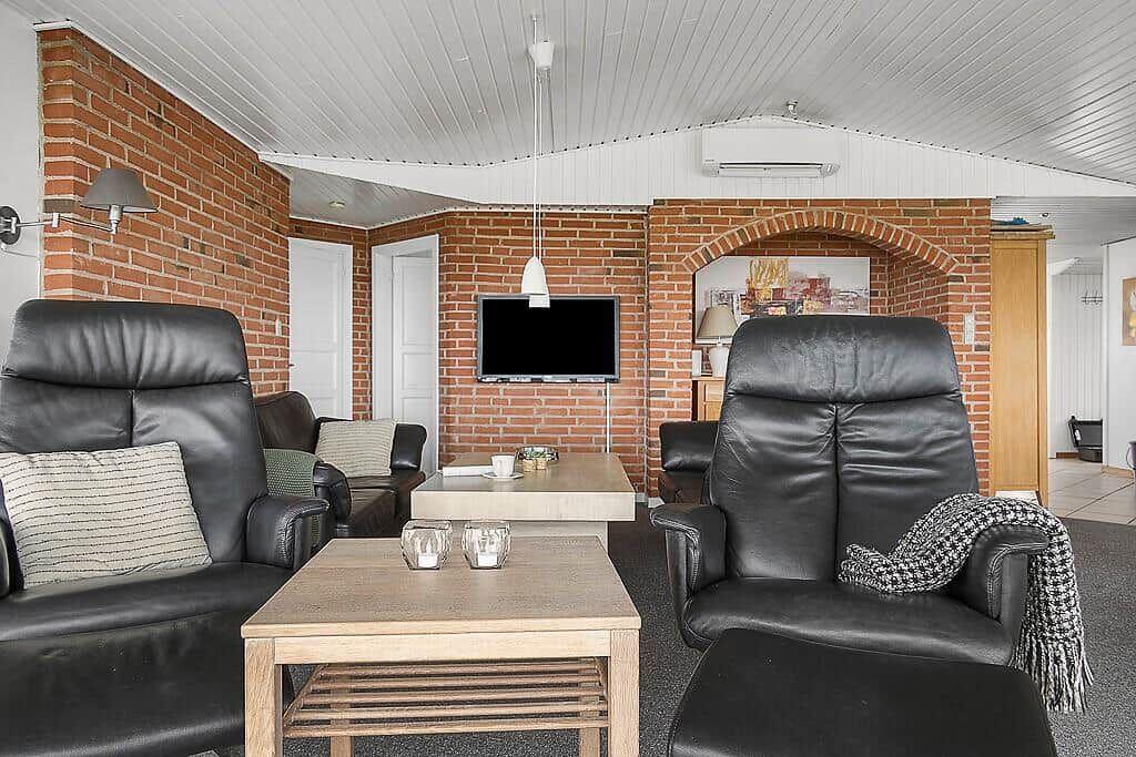 Wohnzimmer mit zwei schwarzen Ledersesseln, Holztisch und Fernseher an Backsteinwand.
