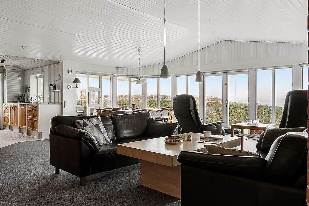 Wohnzimmer mit Ledersofa, Holztisch und Blick auf Felder.