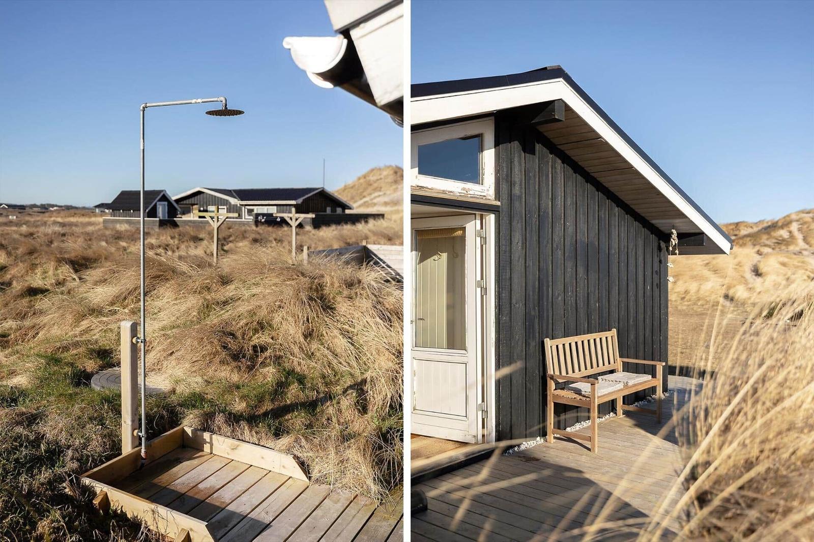 Outdoor shower and wooden deck with bench in front of a black-clad house.