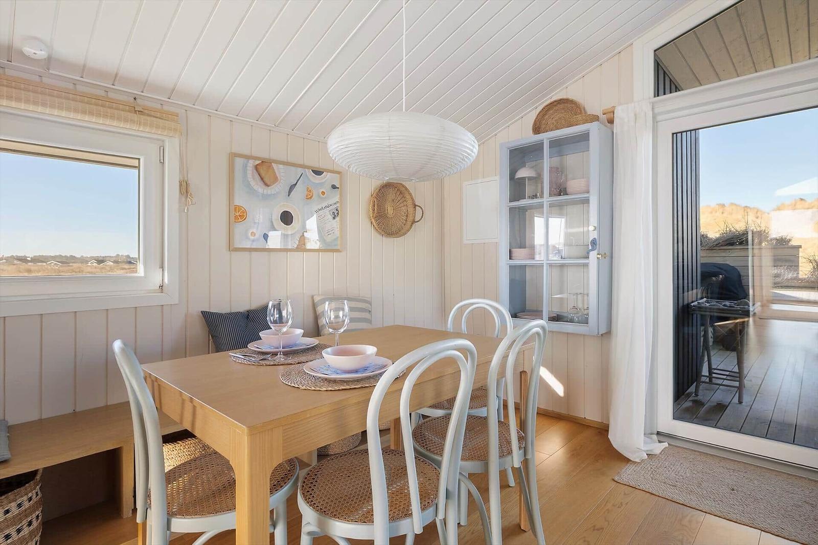 Dining room with wooden table, white chairs, and glass door to terrace.