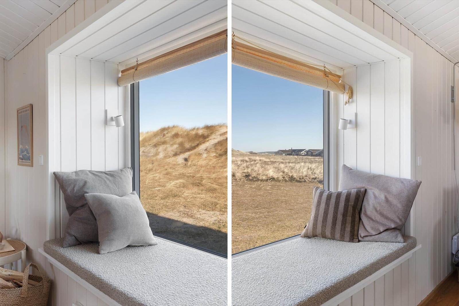 Seating bench with cushions by large window overlooking dunes and vacation homes.