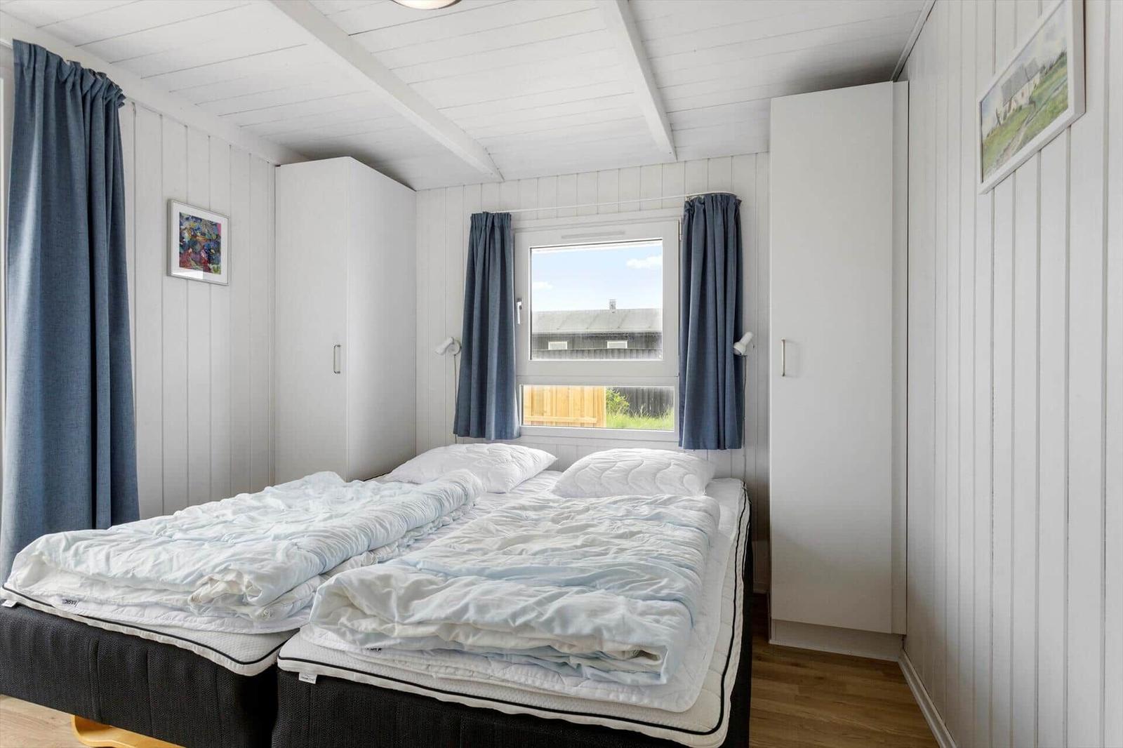 Schlafzimmer mit Doppelbett, Fenster und weißen Schränken.