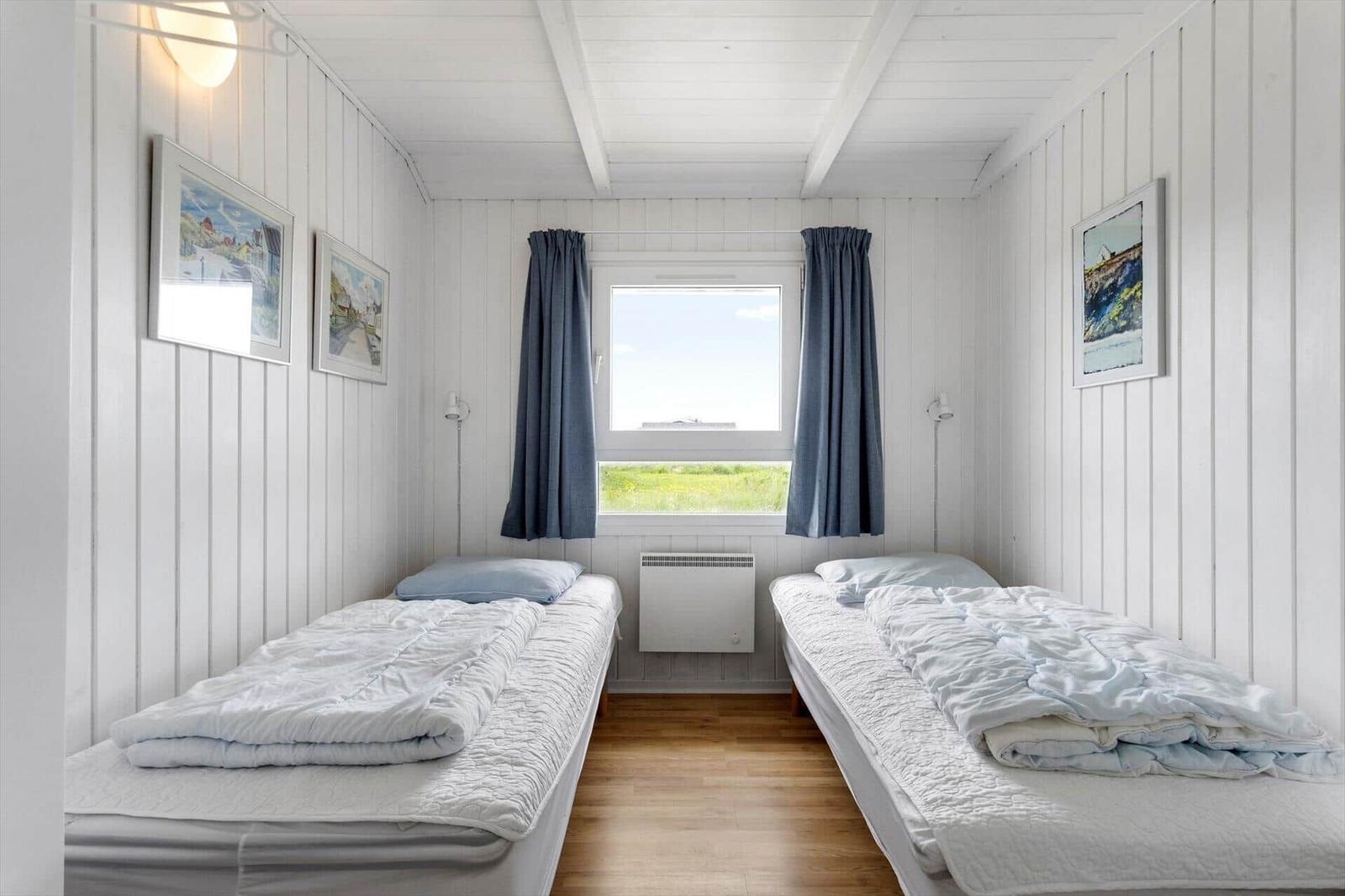 Zwei Betten mit weißen Bettwäsche, Fenster mit blauen Vorhängen und Holzboden.