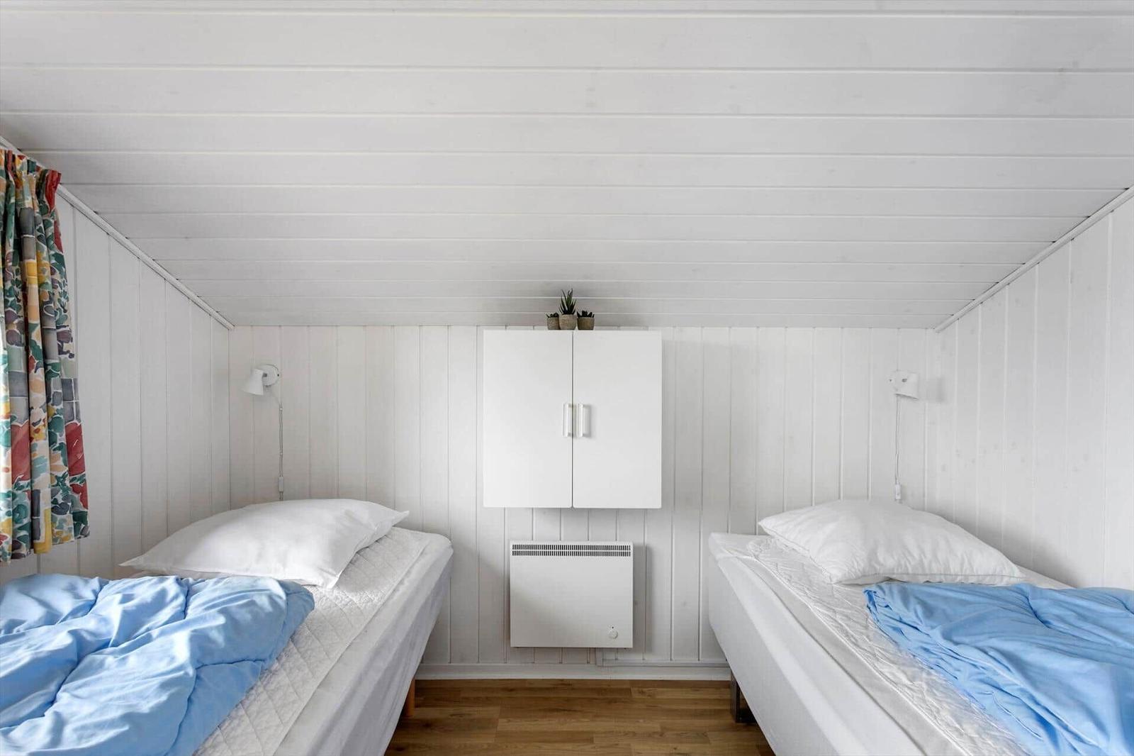 Zwei Betten mit blauen Decken, weißer Wand und Decke, kleiner Schrank und Heizung.