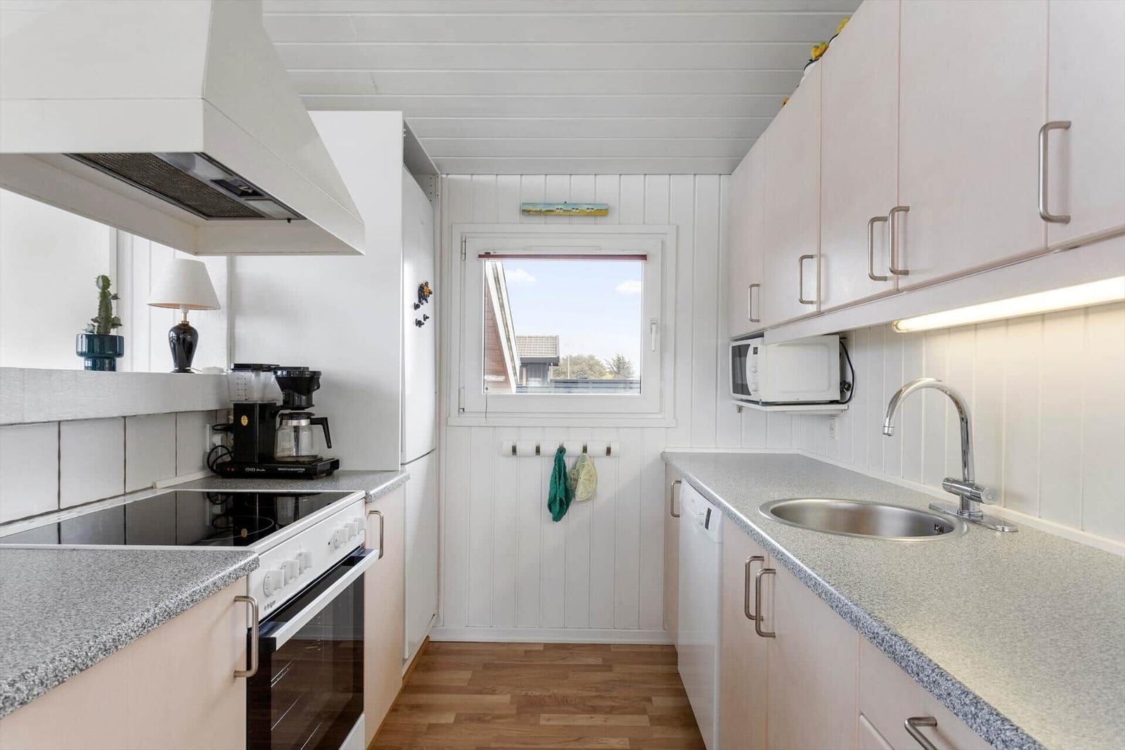 Küche mit Arbeitsplatten, Spüle, Dunstabzug, Kühlschrank und Fenster.