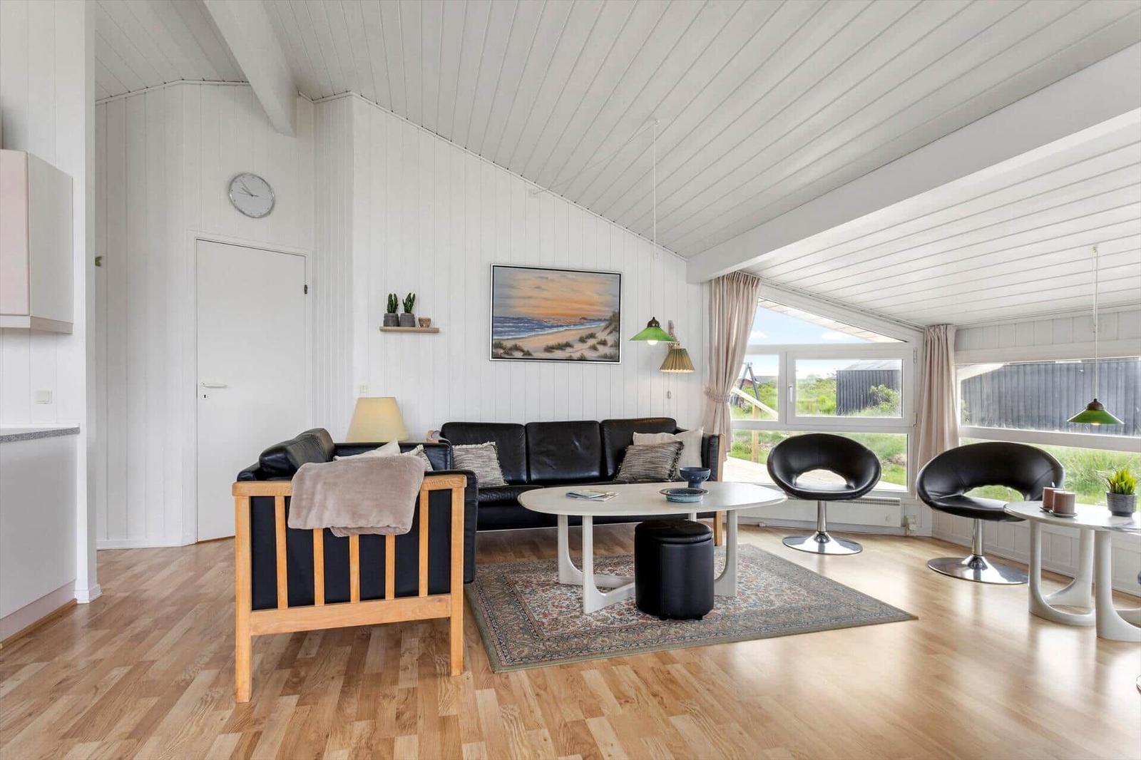 Wohnzimmer mit Sofa, zwei Sesseln und Tisch. Holzfußboden und weiße Wände.