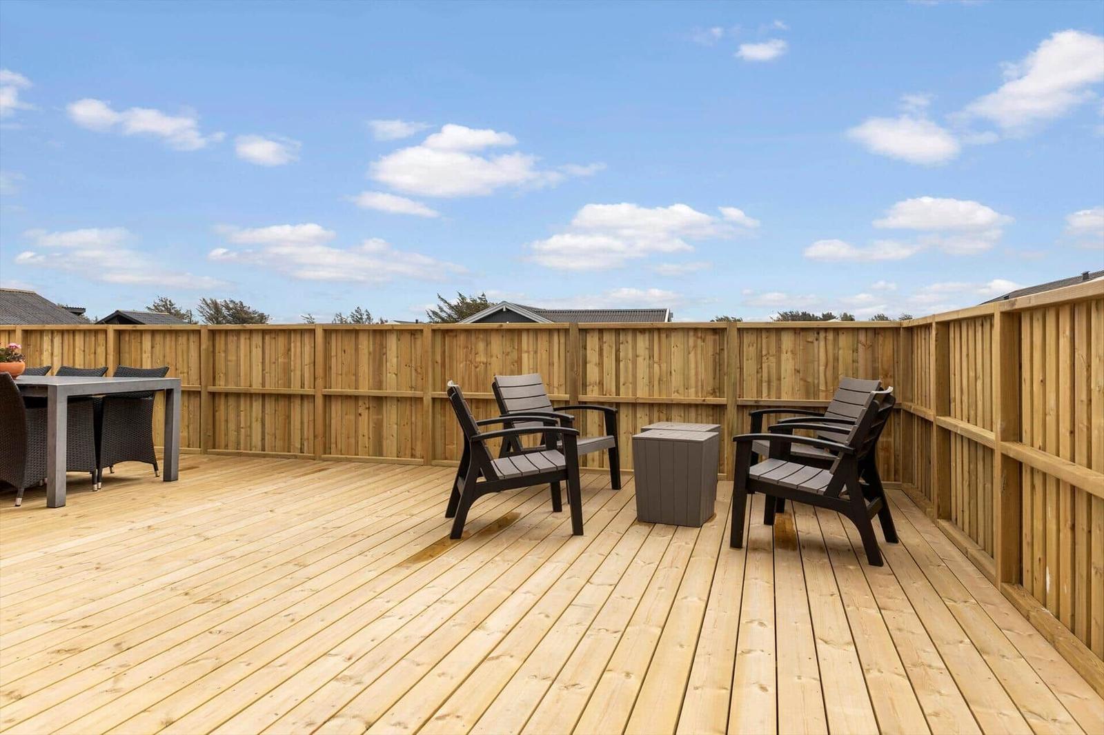 Holzterrasse mit Sitzgelegenheiten und Tisch. Umzäunt mit Holz. Blick auf Himmel und Dächer.
