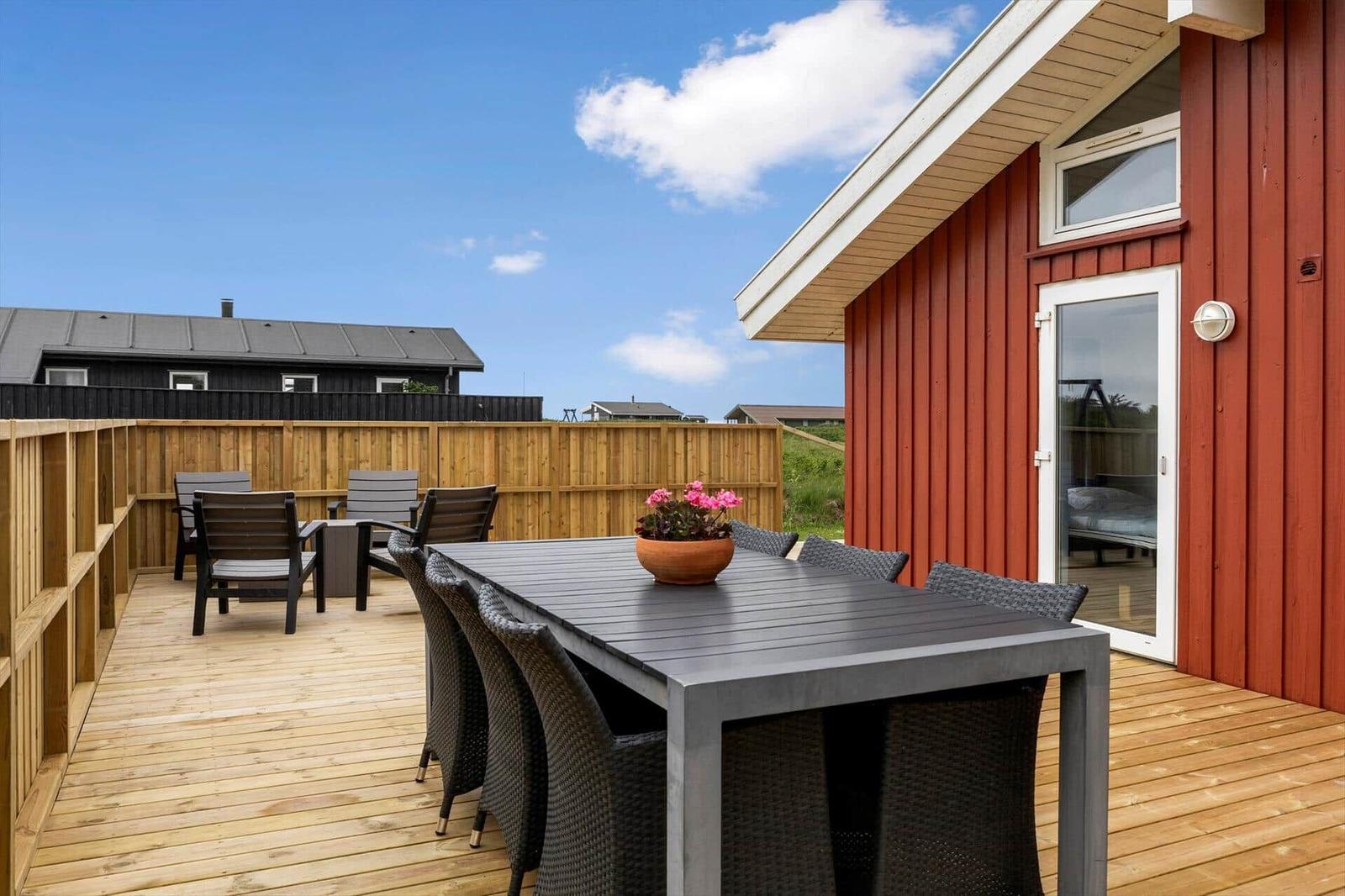 Terrasse mit Tisch und Stühlen, roter Holzhauswand und Blick auf Nachbarhaus.