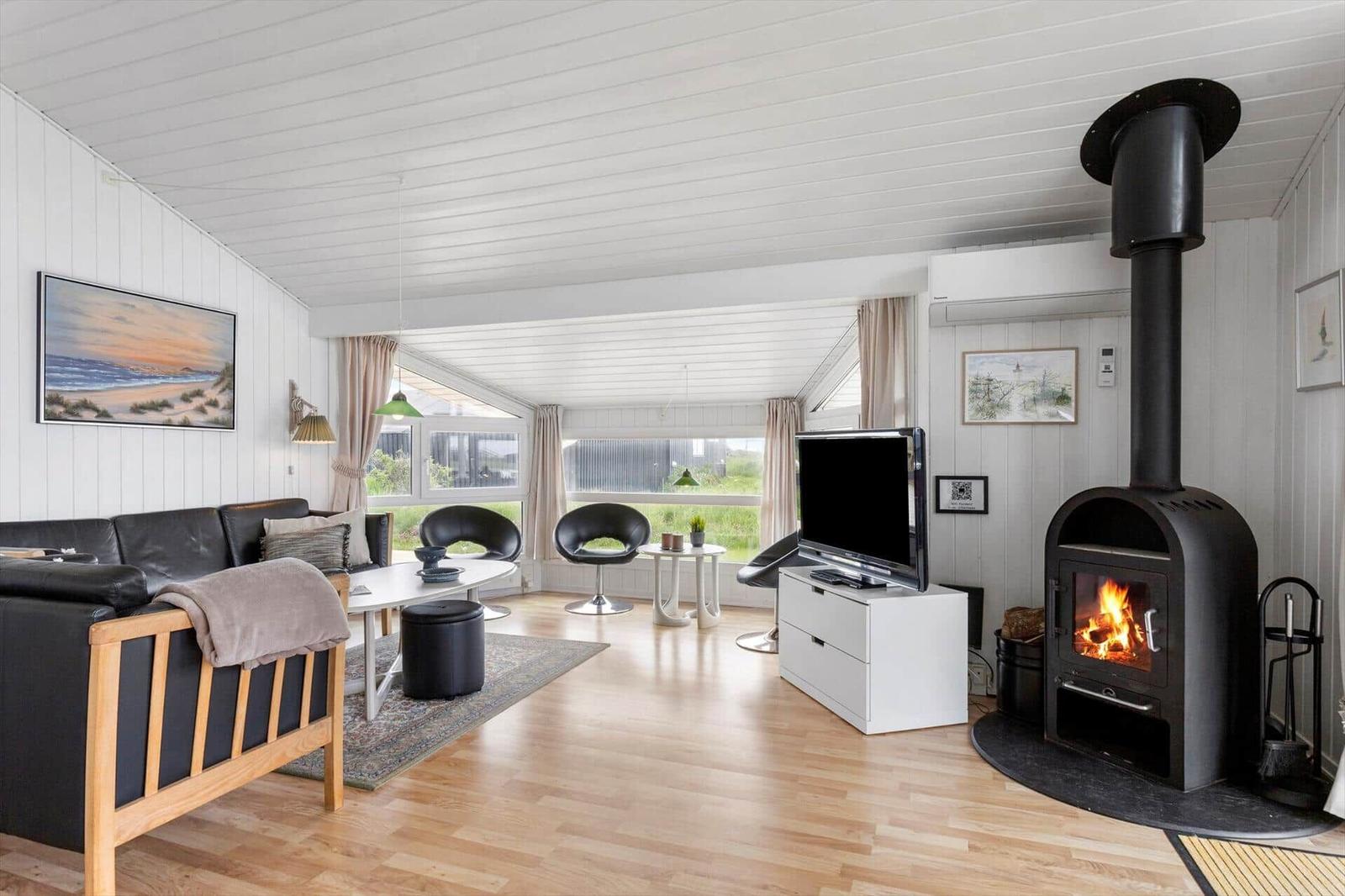 Wohnzimmer mit Kamin, Sofa, TV und Fenstern zum Blick nach draußen.