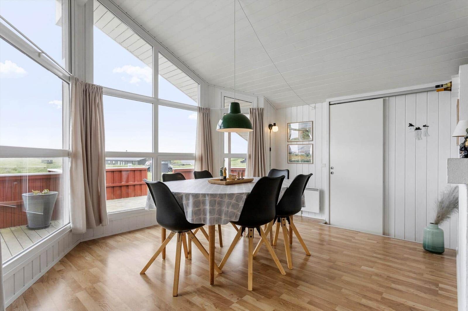 Esszimmer mit Tisch, Stühlen und großen Fenstern. Holzboden und weiße Wände.