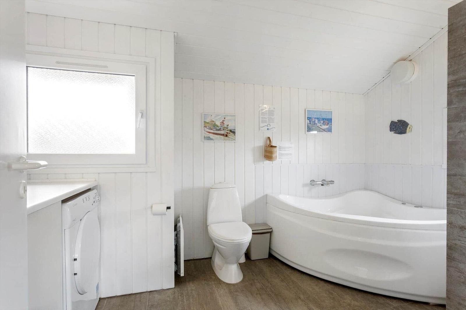 Badezimmer mit Badewanne, Toilette und Waschmaschine. Weiße Wände und Holzboden.