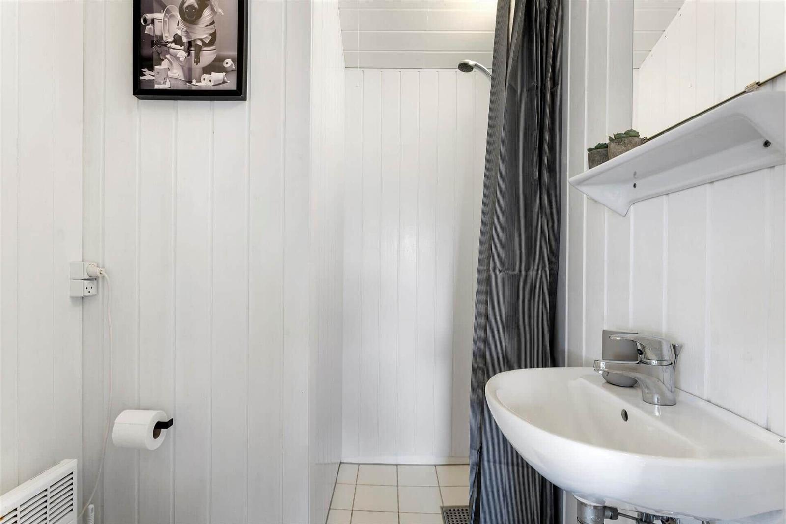 Badezimmer mit Waschbecken, Dusche und Toilette. Weiße Wände und graue Duschvorhang.