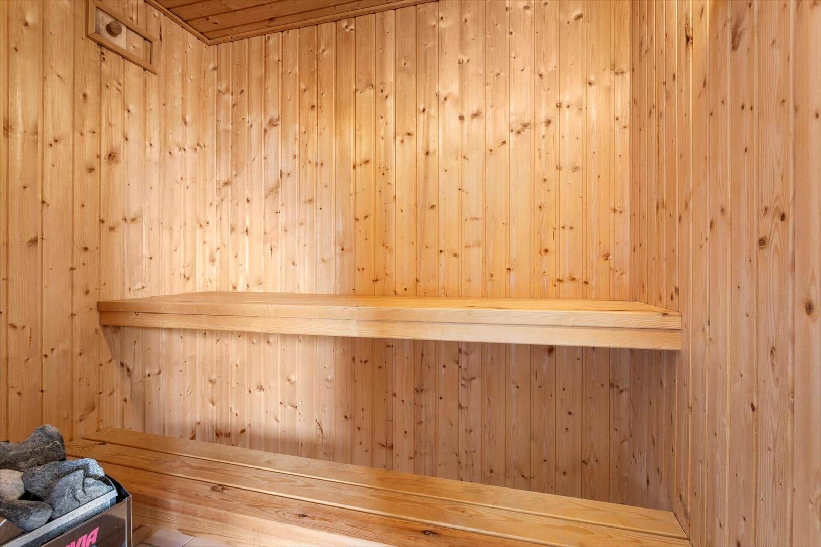 Sauna mit Holzwänden und zwei Sitzbänken. Im Vordergrund ist ein Steinkasten mit Steinen.