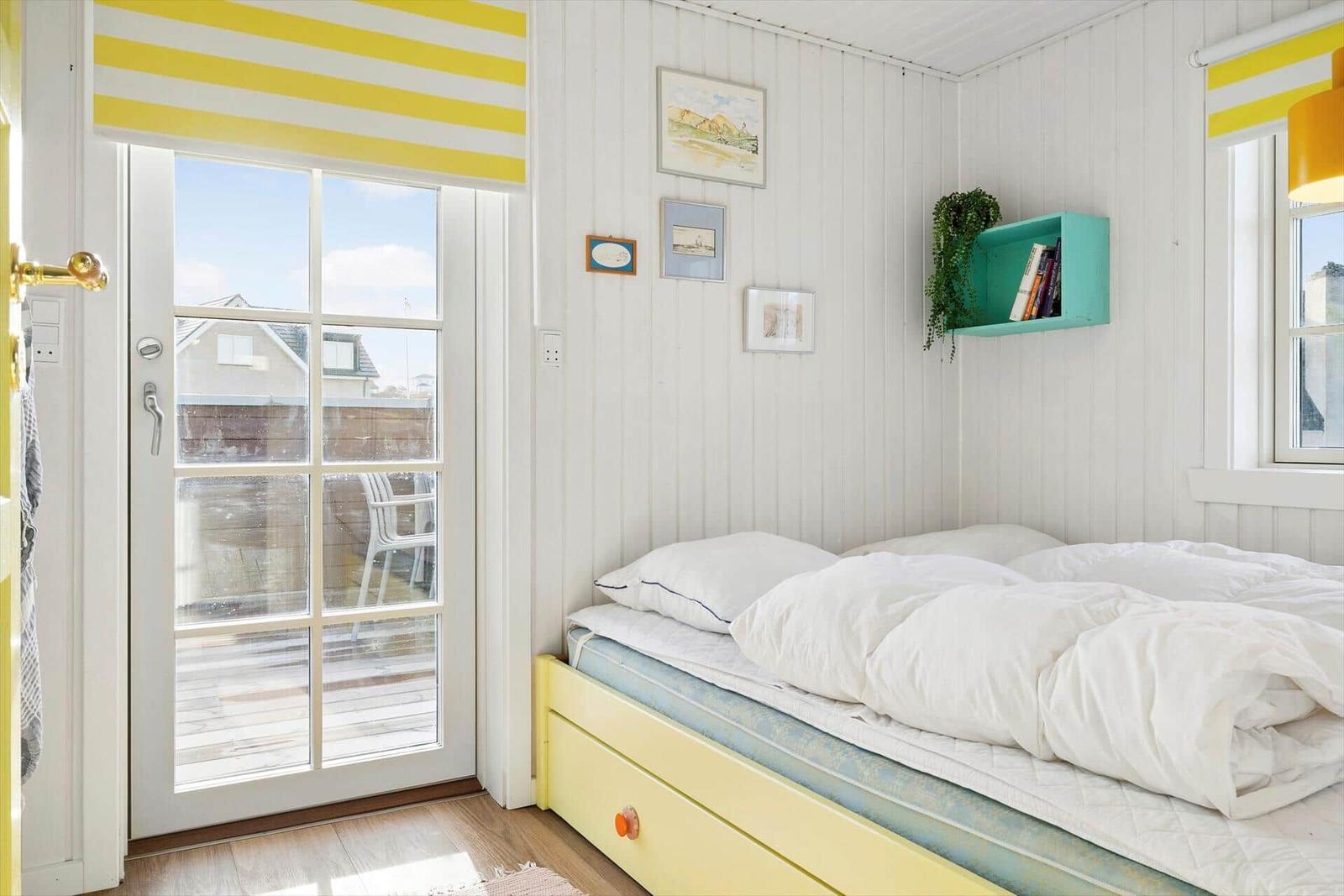 Bedroom with bed, windows, and door. Wall with pictures and green shelf.