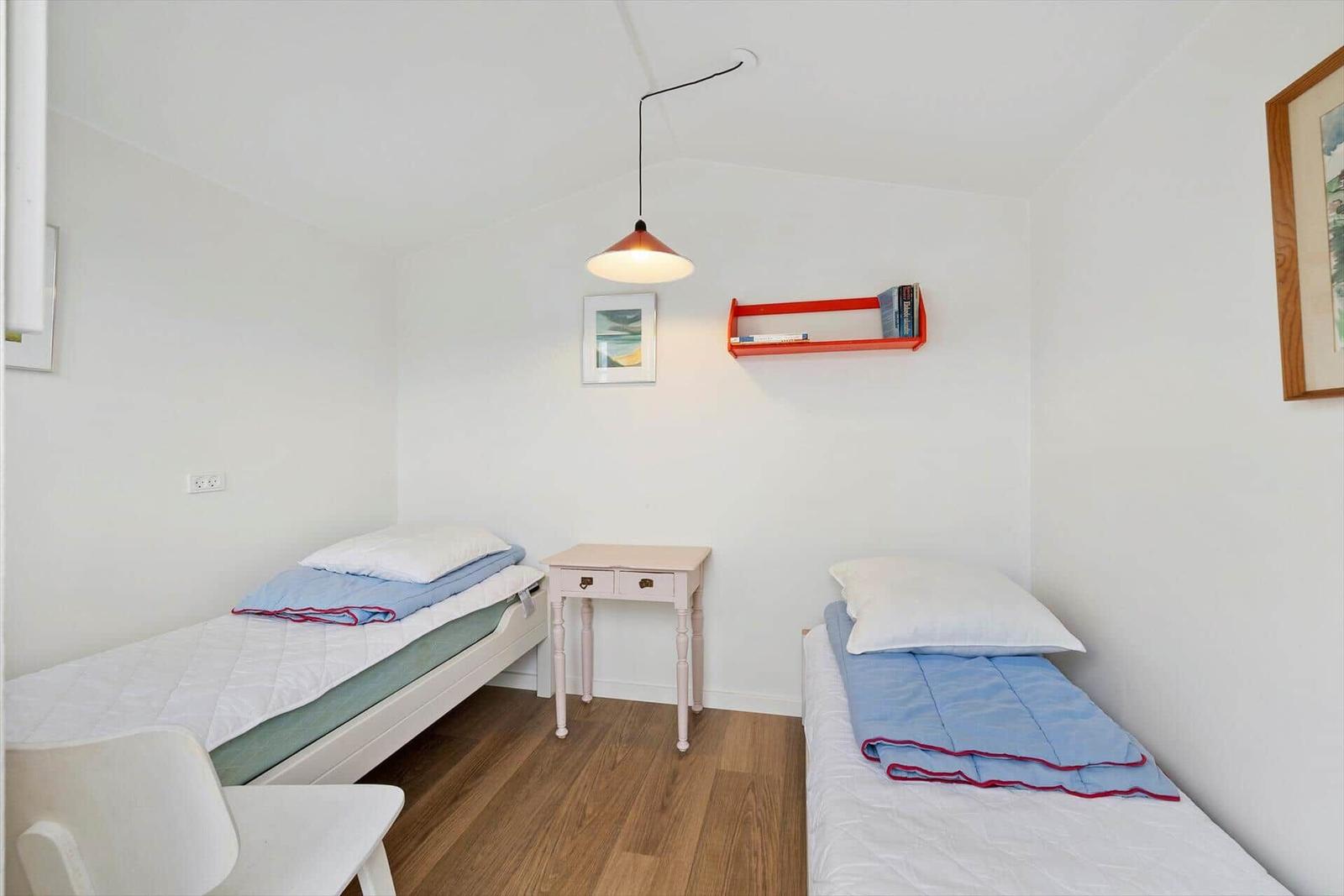 Two single beds, nightstand, and wall shelf with books.