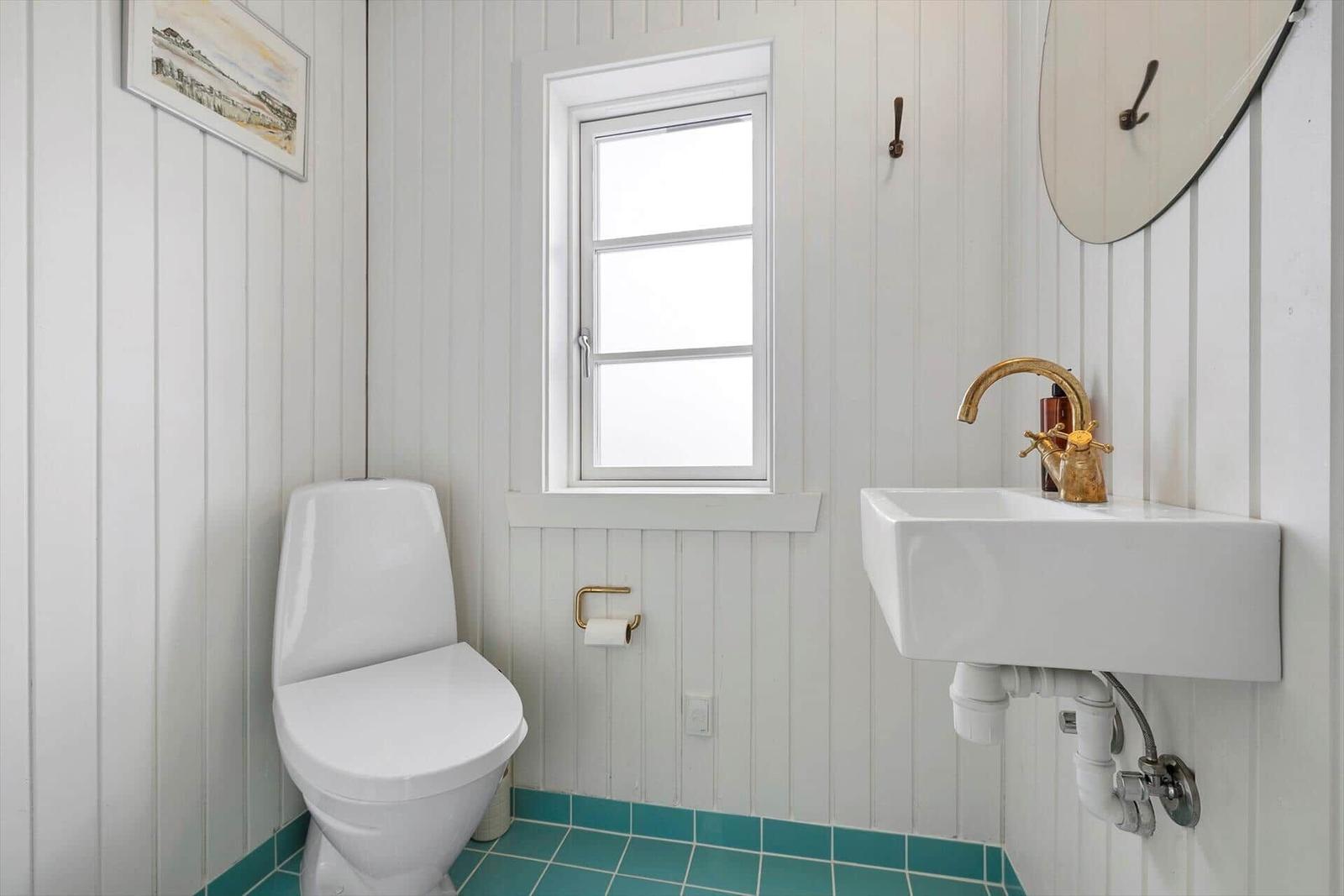 Bathroom with toilet, sink, and window. Panelled walls and turquoise floor.
