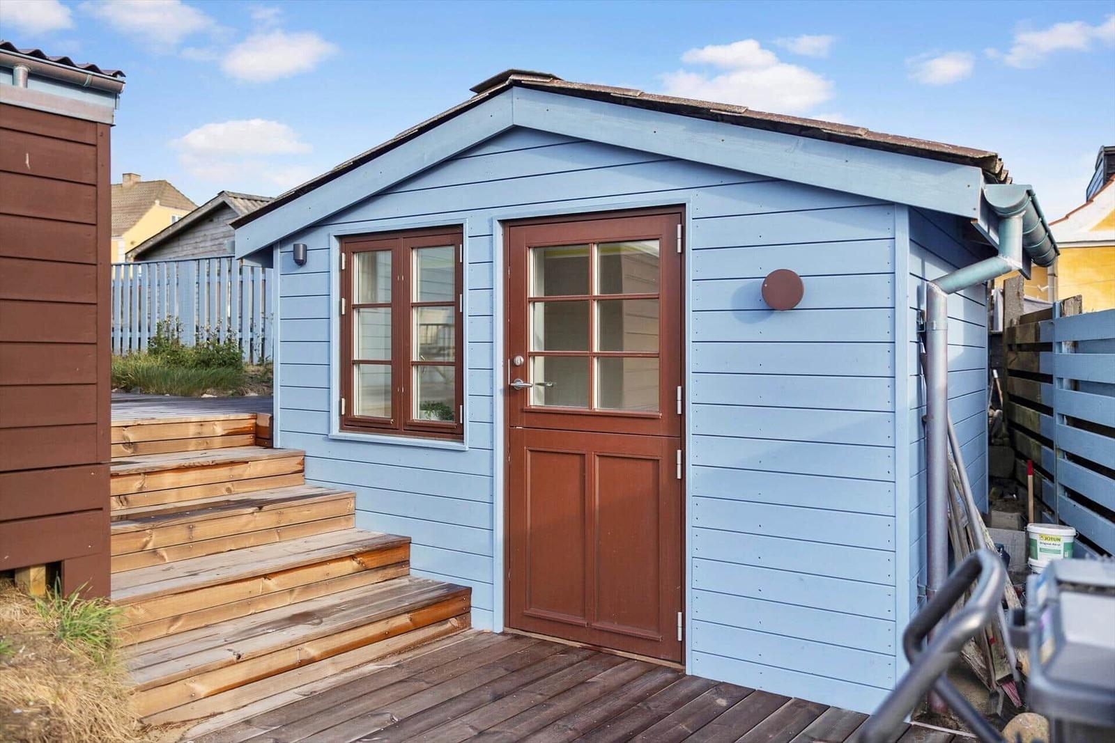 A small blue wooden house with brown door and windows. Wooden terrace with steps.