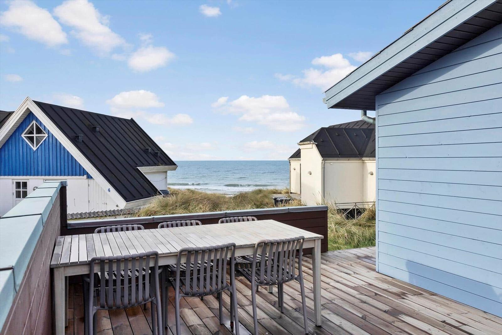 Deck with table and chairs offers view of sea and beach houses.