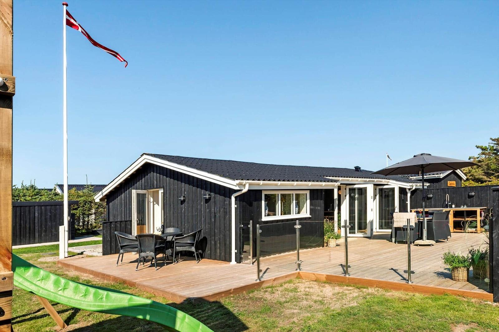 Ein schwarzes Haus mit Terrasse und dänischer Flagge. Gartenmöbel und Sonnenschirm.