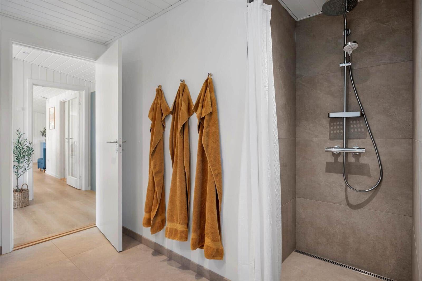 Dusche mit Duschbrause und drei gelbe Handtücher an der Wand.