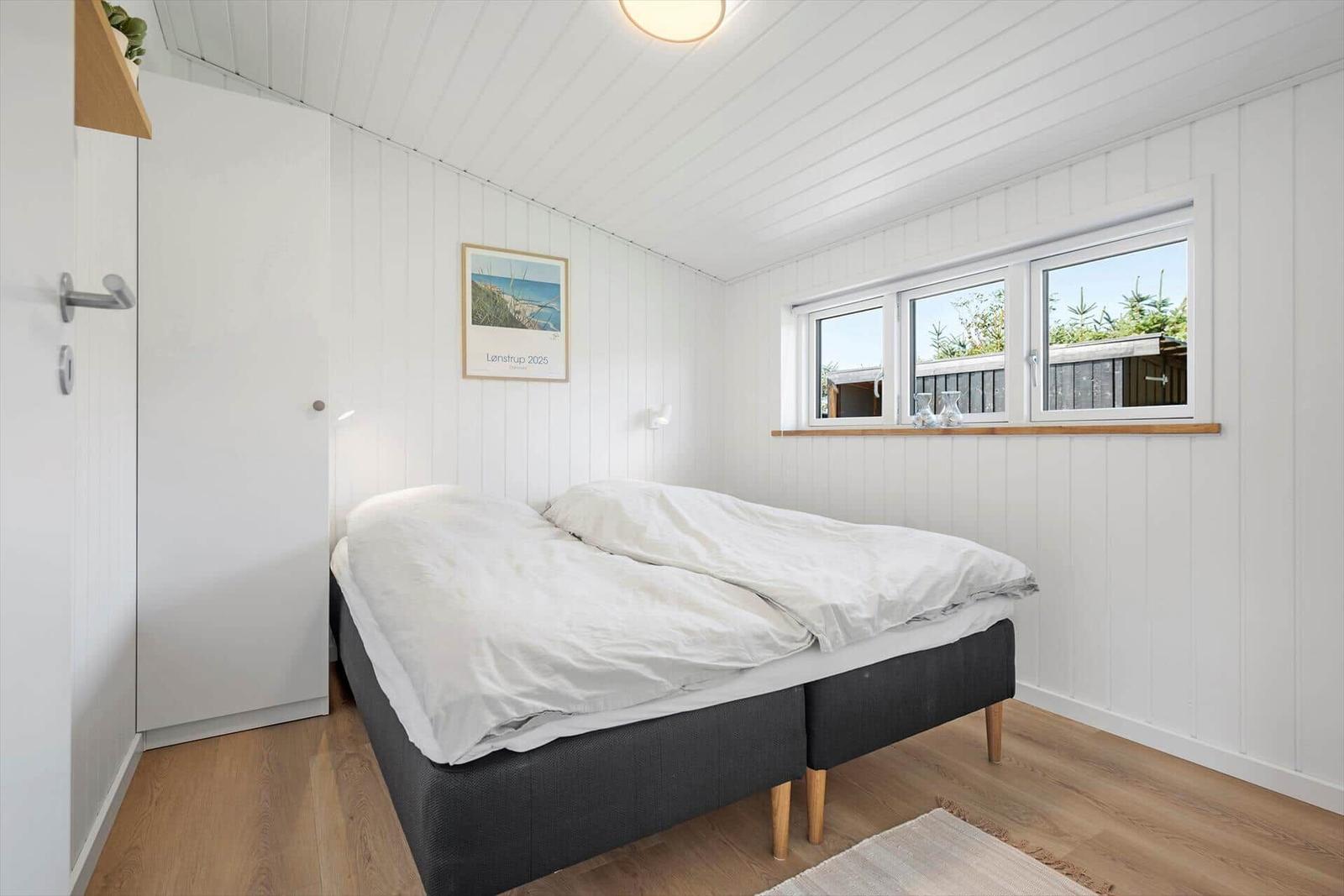 Schlafzimmer mit Doppelbett, weißen Wänden und Fensterblick.