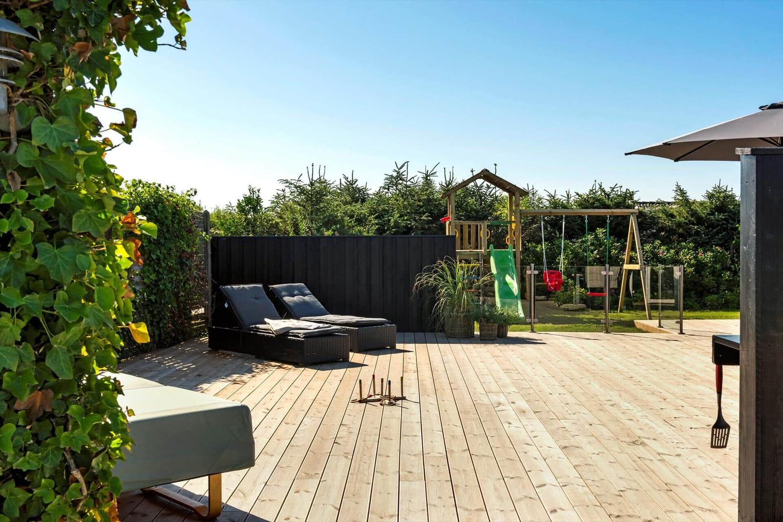 Holzterrasse mit Liegestühlen, Spielplatz und Grillbereich im Garten.