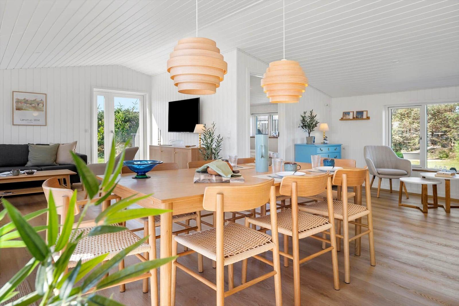 Esszimmer mit Holztisch, Stühlen und hängenden Lampen. Wohnbereich mit Sofa und TV.