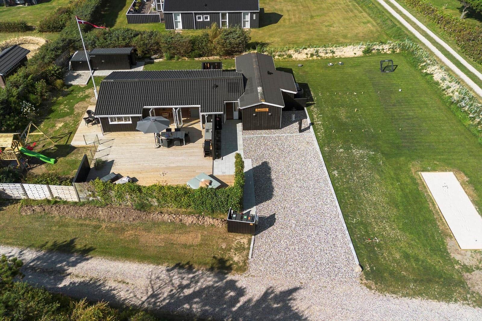 Haus mit großem Garten, Terrasse und Spielplatz. Gravelweg und Flagge sichtbar.