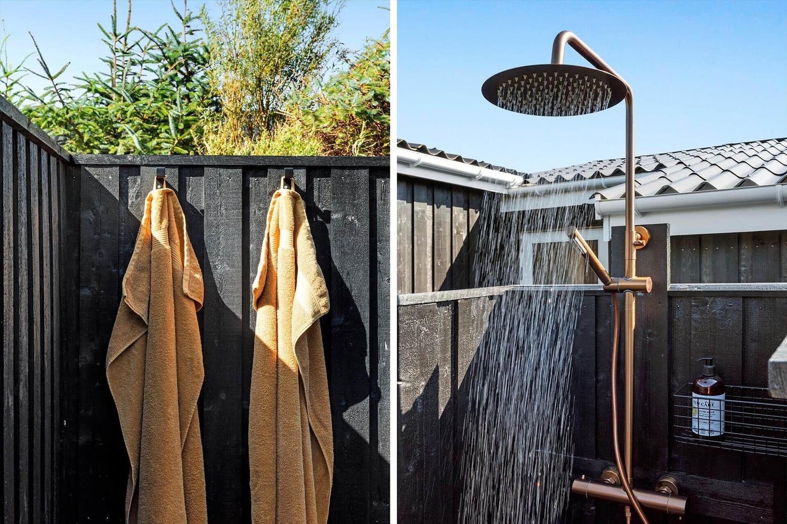 Zwei goldene Handtücher hängen an einem schwarzen Zaun. Eine Dusche mit goldener Armatur und Wasserstrahl.
