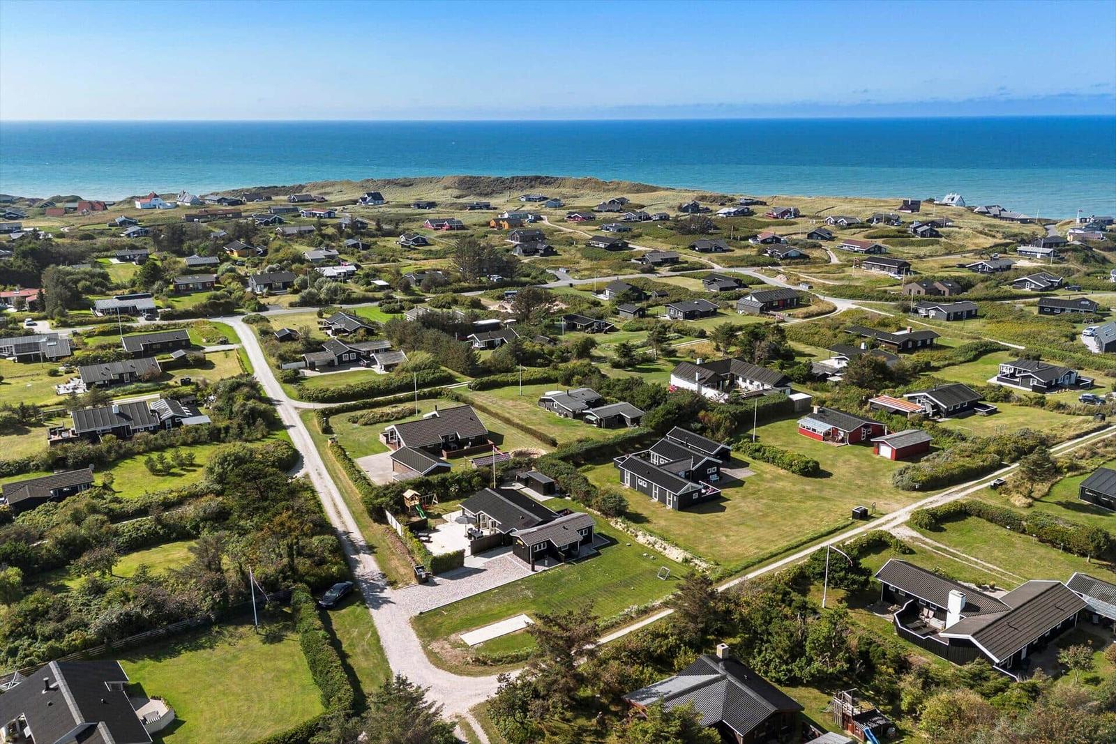 Aerial view of coastal village with houses, green lawns, and ocean in background.