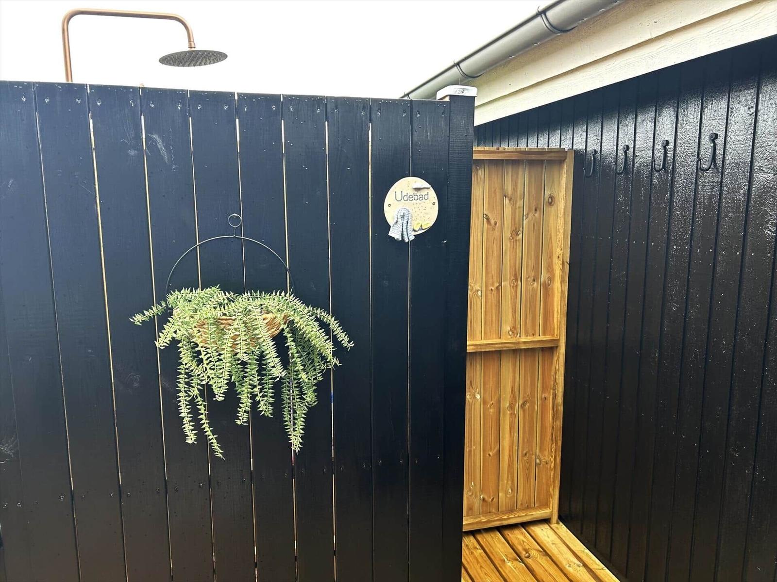 Außenbad mit Dusche, Pflanze und Holztür.