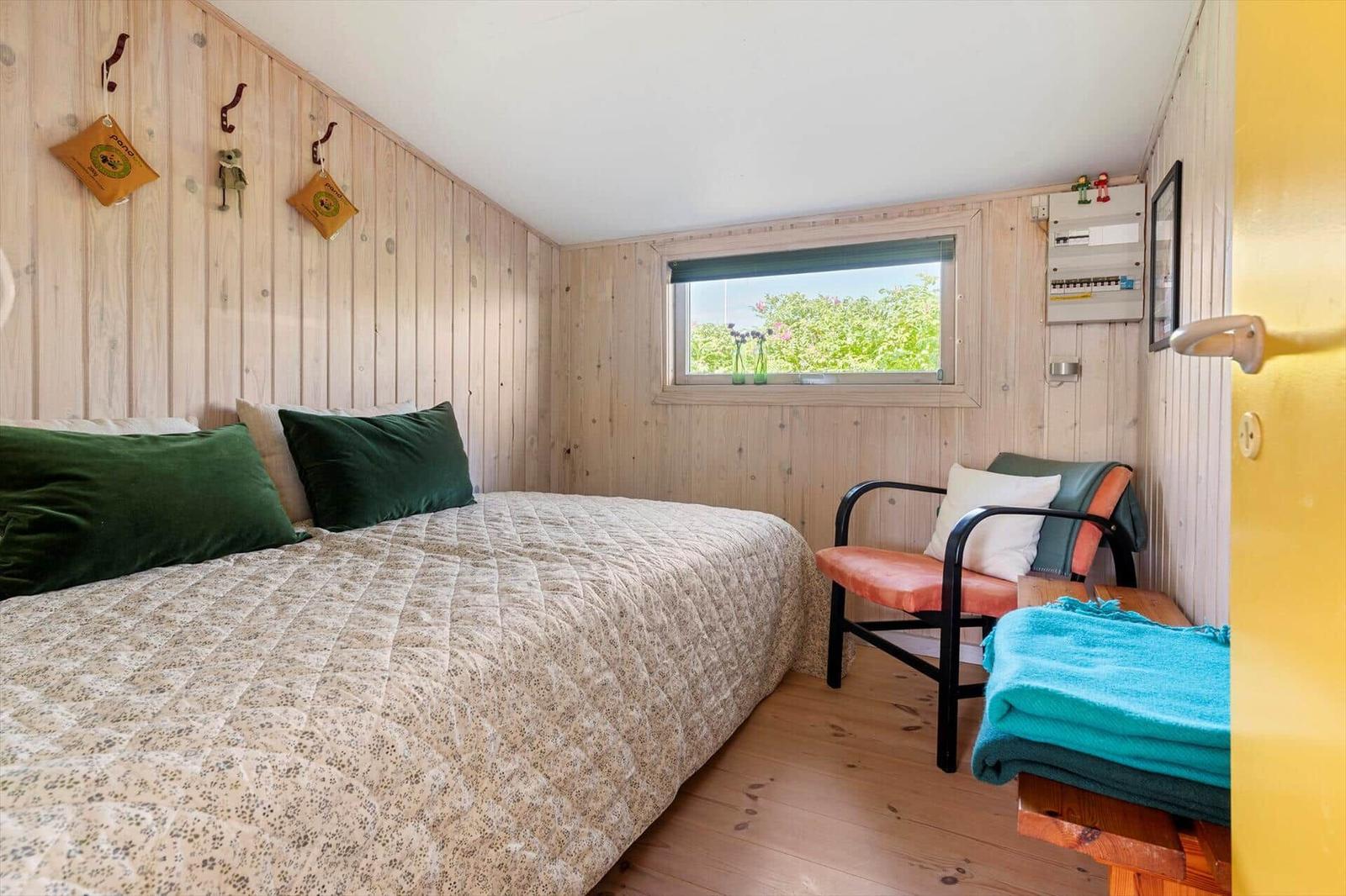 Schlafzimmer mit Bett, Stuhl und Fenster mit Blick auf Grün.