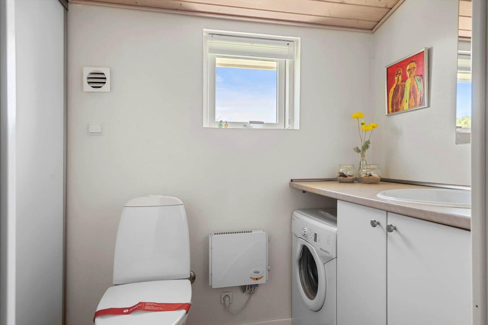 Toilette, Waschmaschine und Waschbecken mit Fenster und Bild.