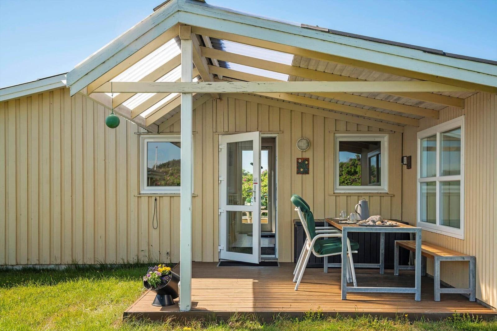 Haus mit Terrasse, Tisch, Stühlen und grünem Hängemobil.