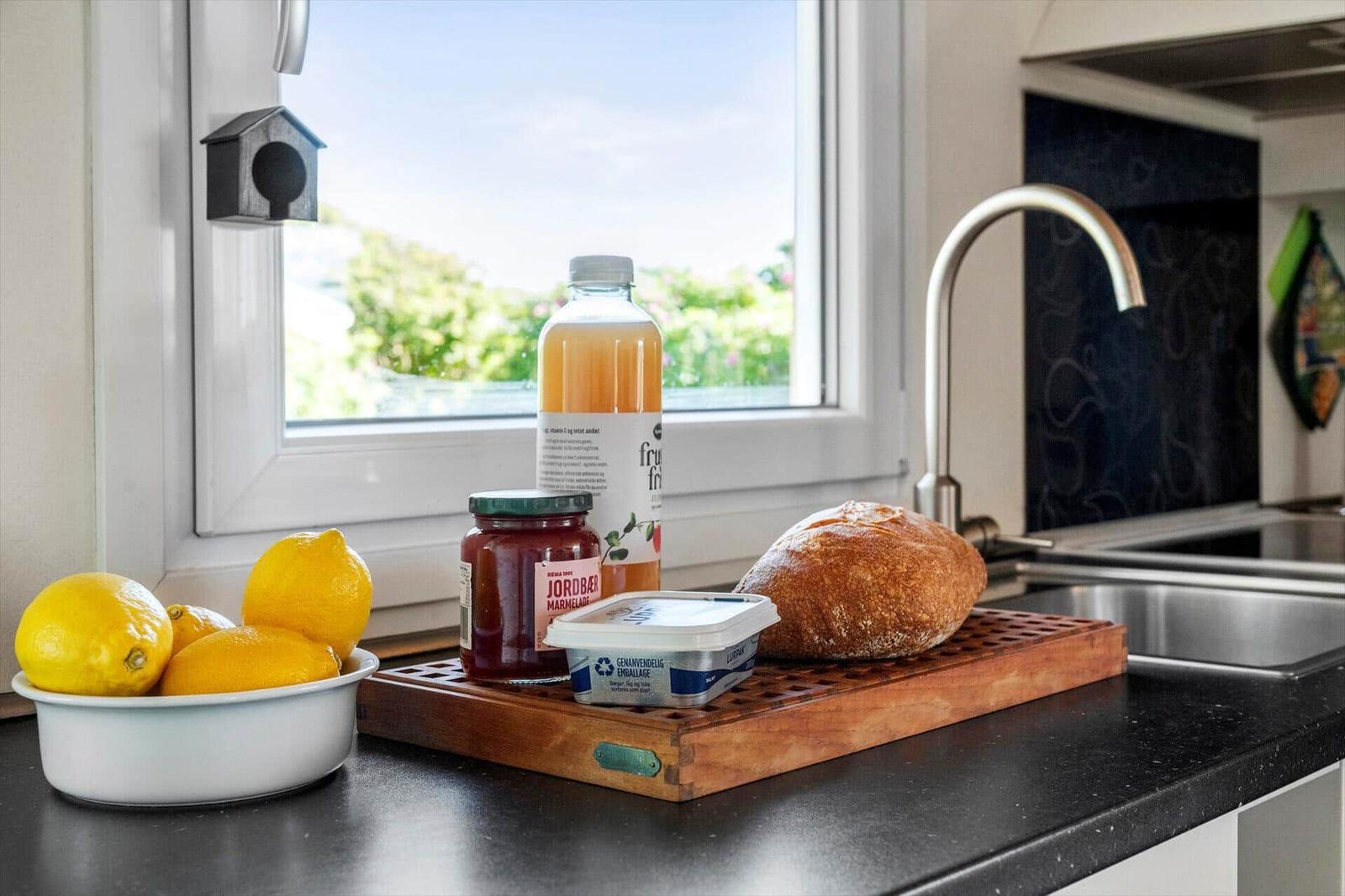 Küchenfenster mit Blick auf Garten, darauf Obst, Brot und Flasche.