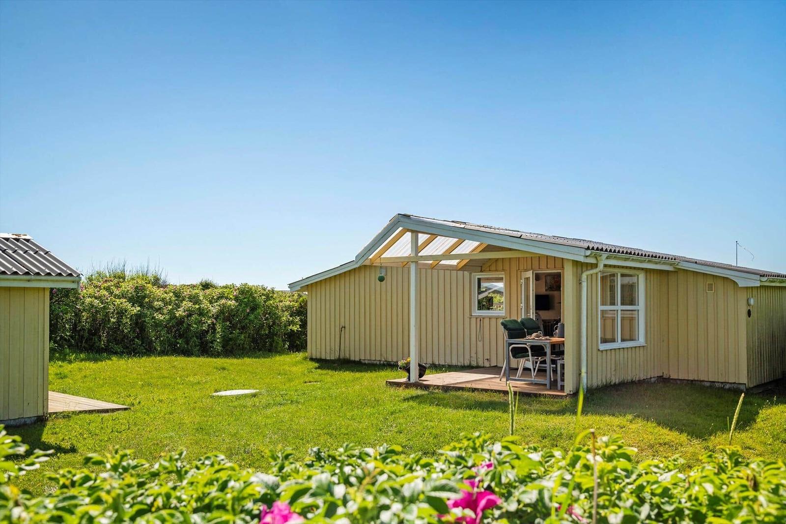 Haus mit Terrasse, Garten und blauem Himmel. Tisch und Stühle stehen draußen.