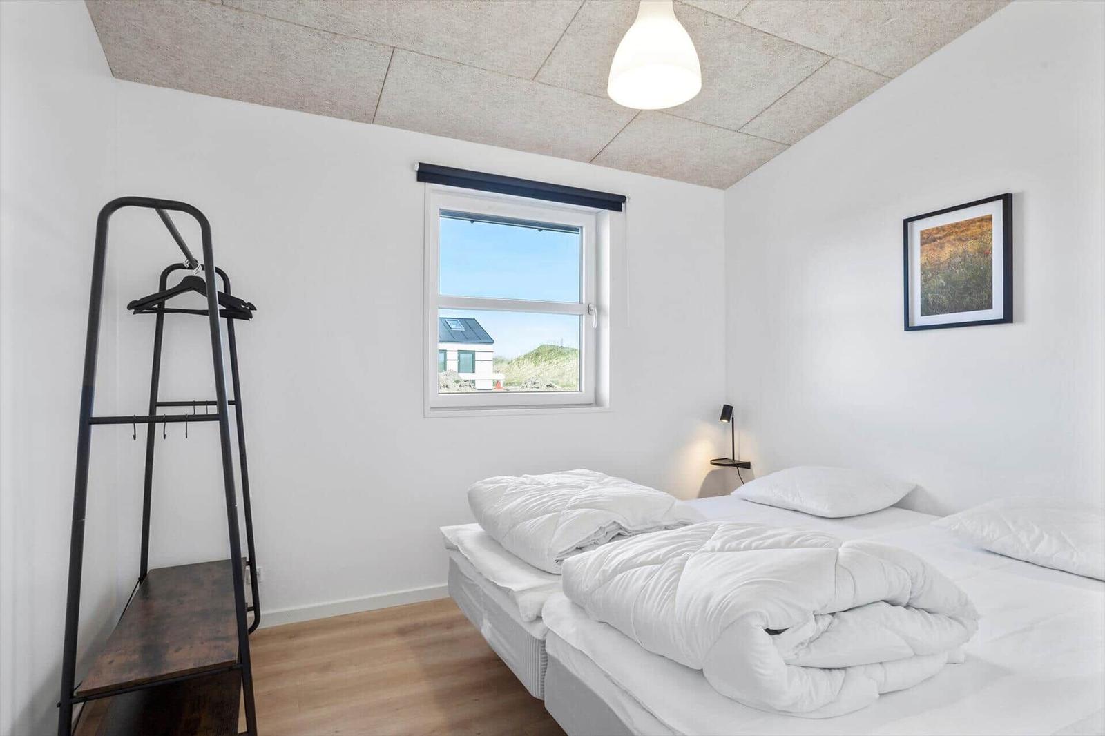 Bedroom with bed, coat rack, and window overlooking the landscape.