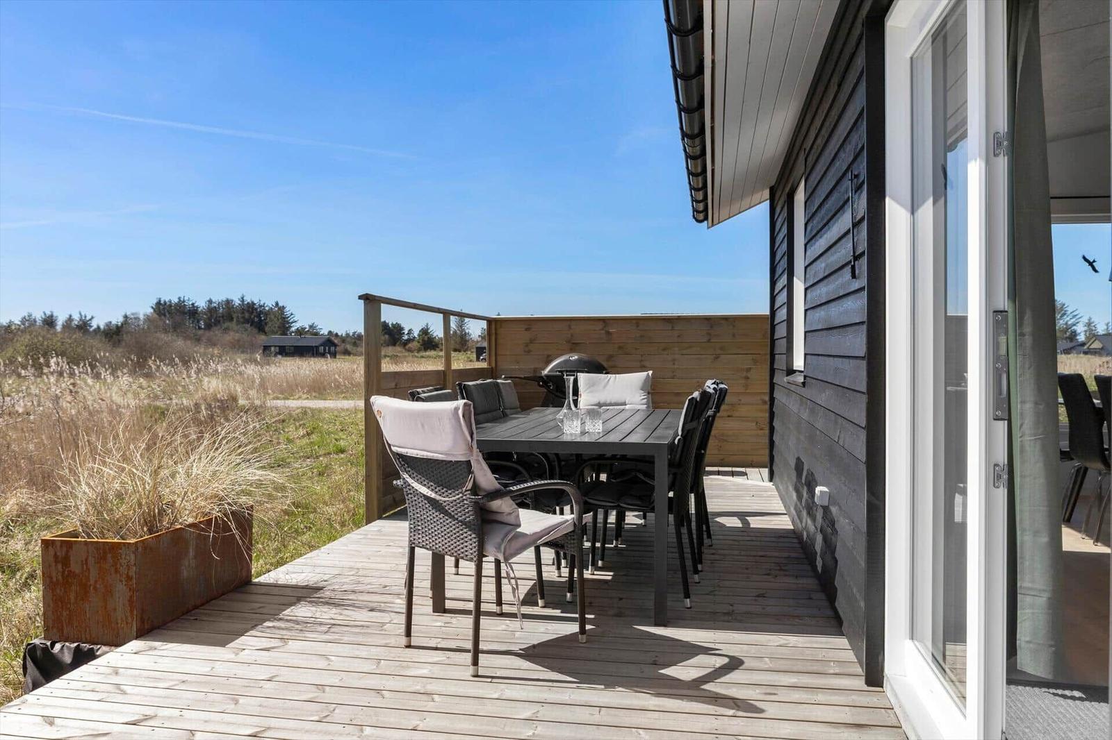 Deck with table, chairs, and grill. Wooden railing and plant. View of field and forest.