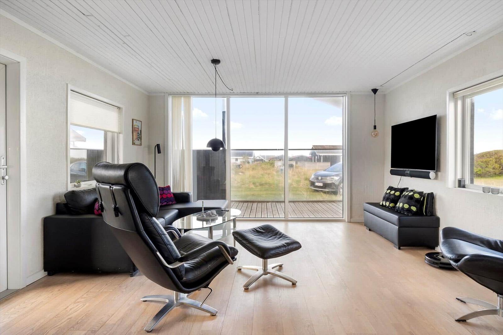 Living room with black leather furniture, wooden floor, and large window to terrace.