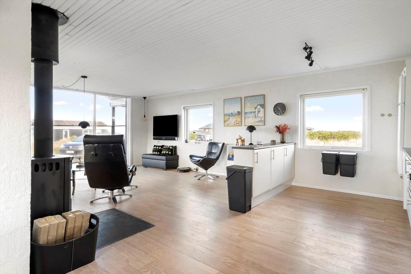 Living room with wooden floor, black chairs, TV, and windows with views outside.
